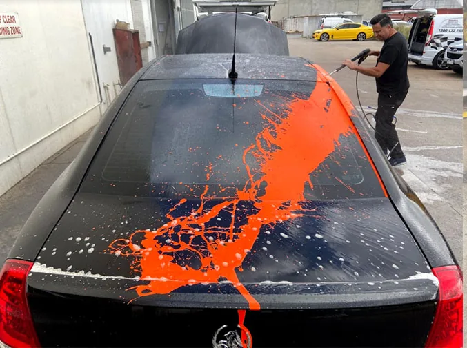 Black sedan covered in orange paint overspray across the roof and boot